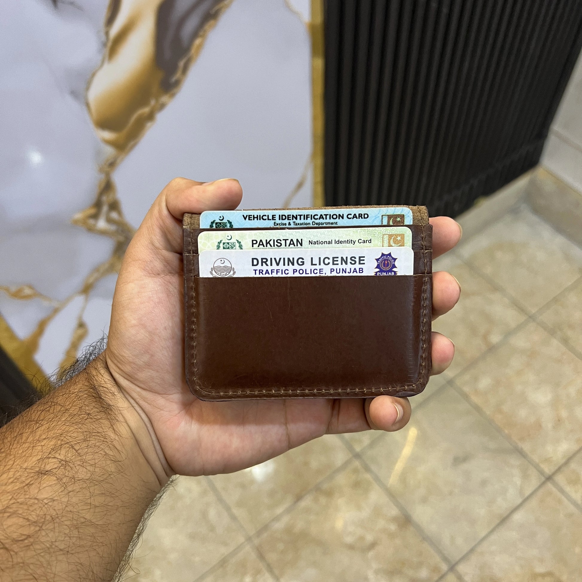Hand holding a brown wallet with a Pakistan driving license and vehicle identification card.