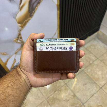 Hand holding a brown wallet with a Pakistan driving license and vehicle identification card.