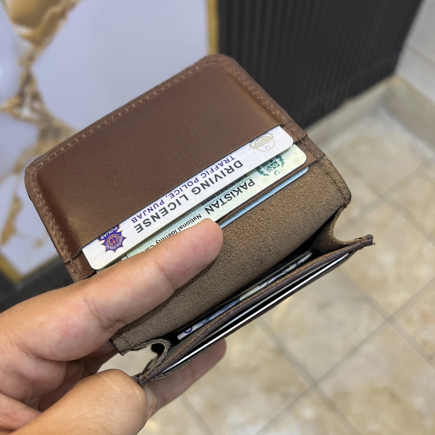 Brown wallet with a driver's license card held by a hand on a blurred background