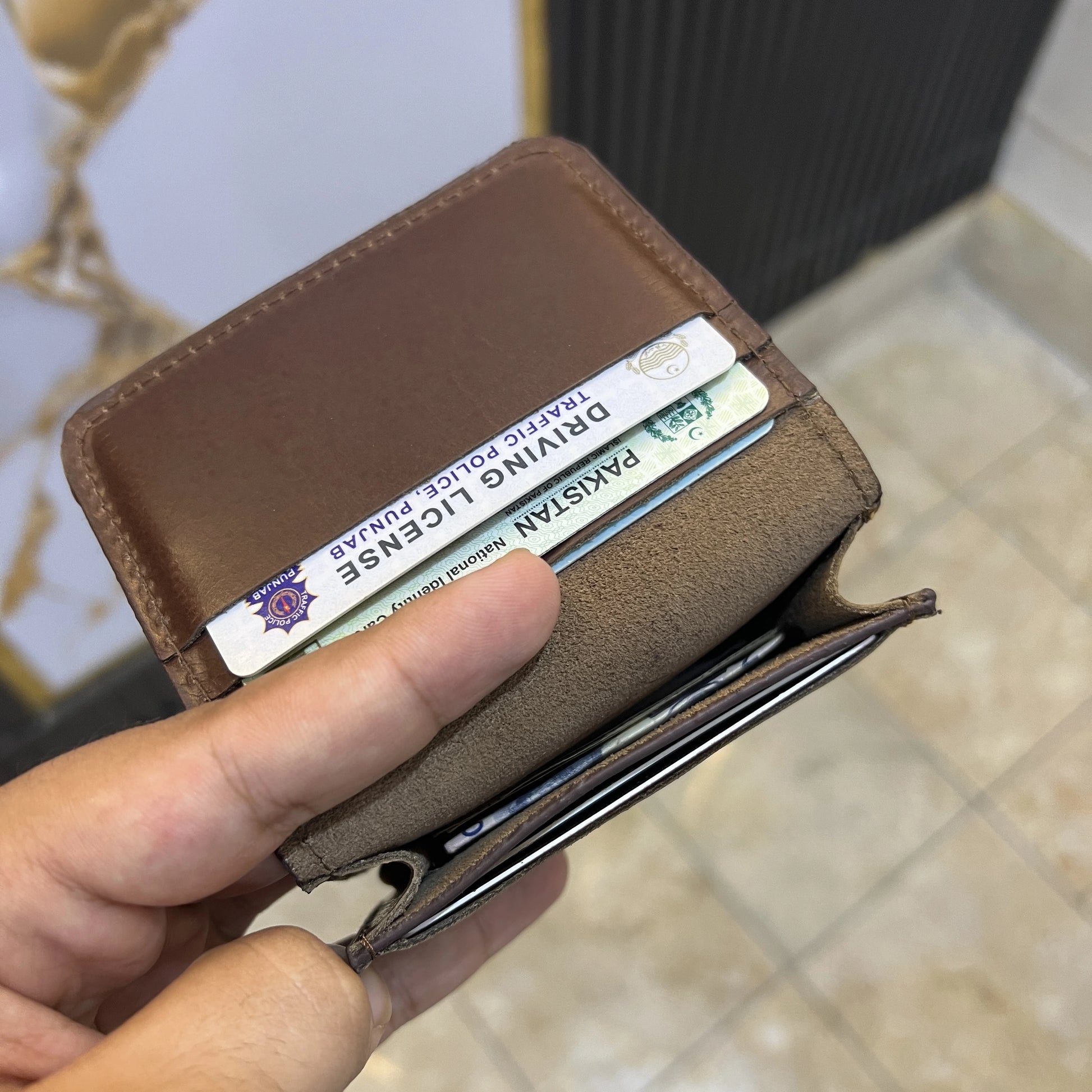 Brown wallet with a driver's license card held by a hand on a blurred background