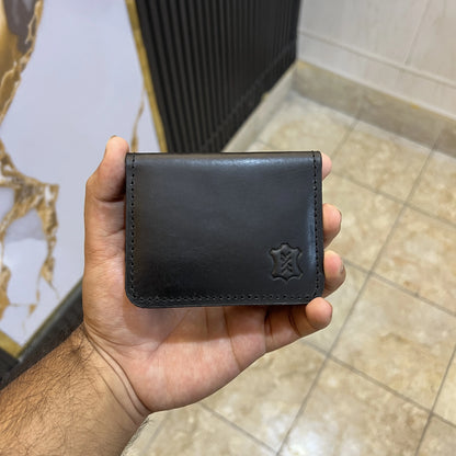 Hand holding a black leather wallet with a brand logo against a tiled floor background