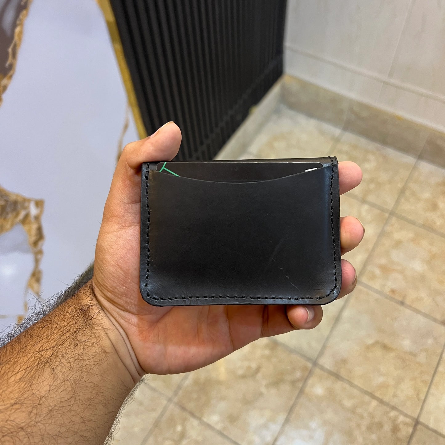 Hand holding a black leather wallet against a bathroom background