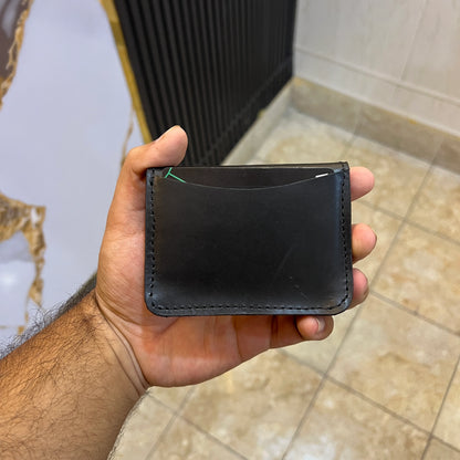 Hand holding a black leather wallet against a bathroom background