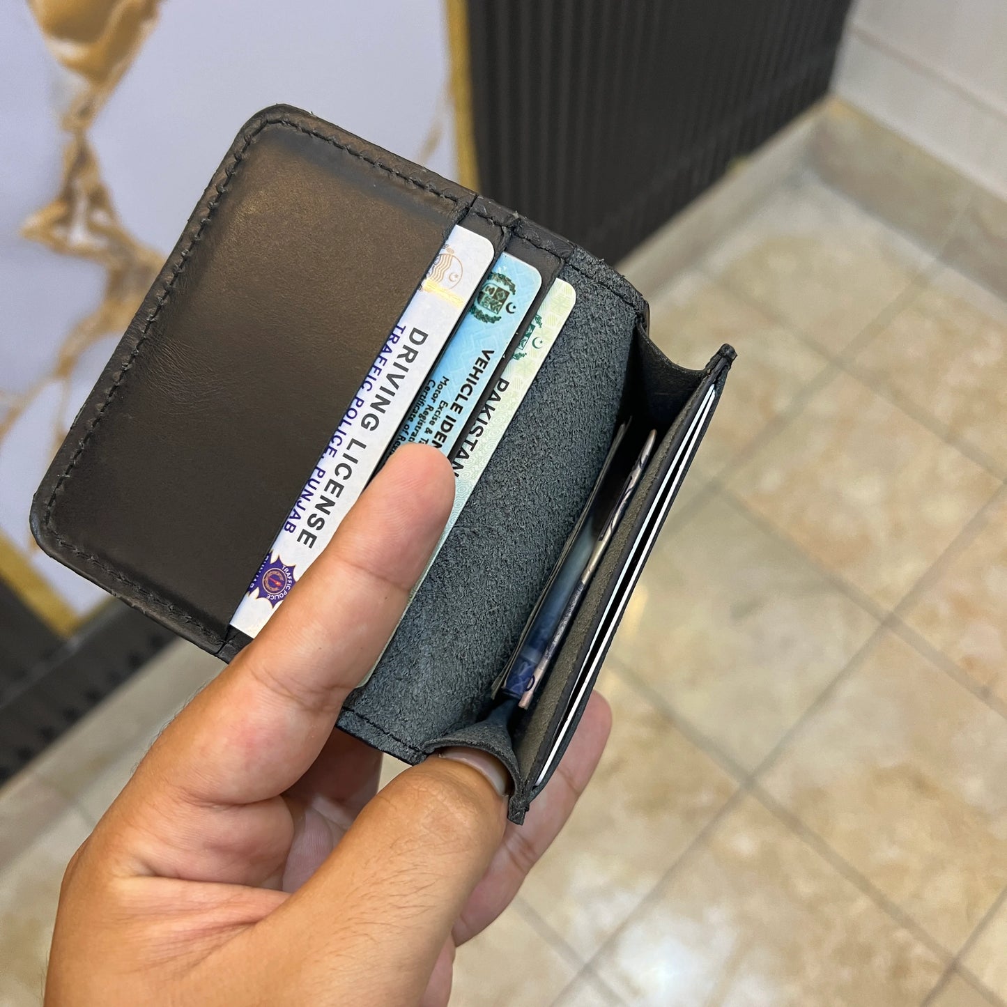 Hand holding a leather wallet with cards, including a driving license, against a blurred background.