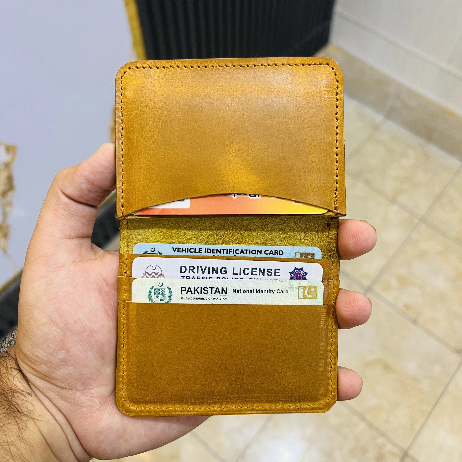 Hand holding a brown leather wallet with identification cards inside