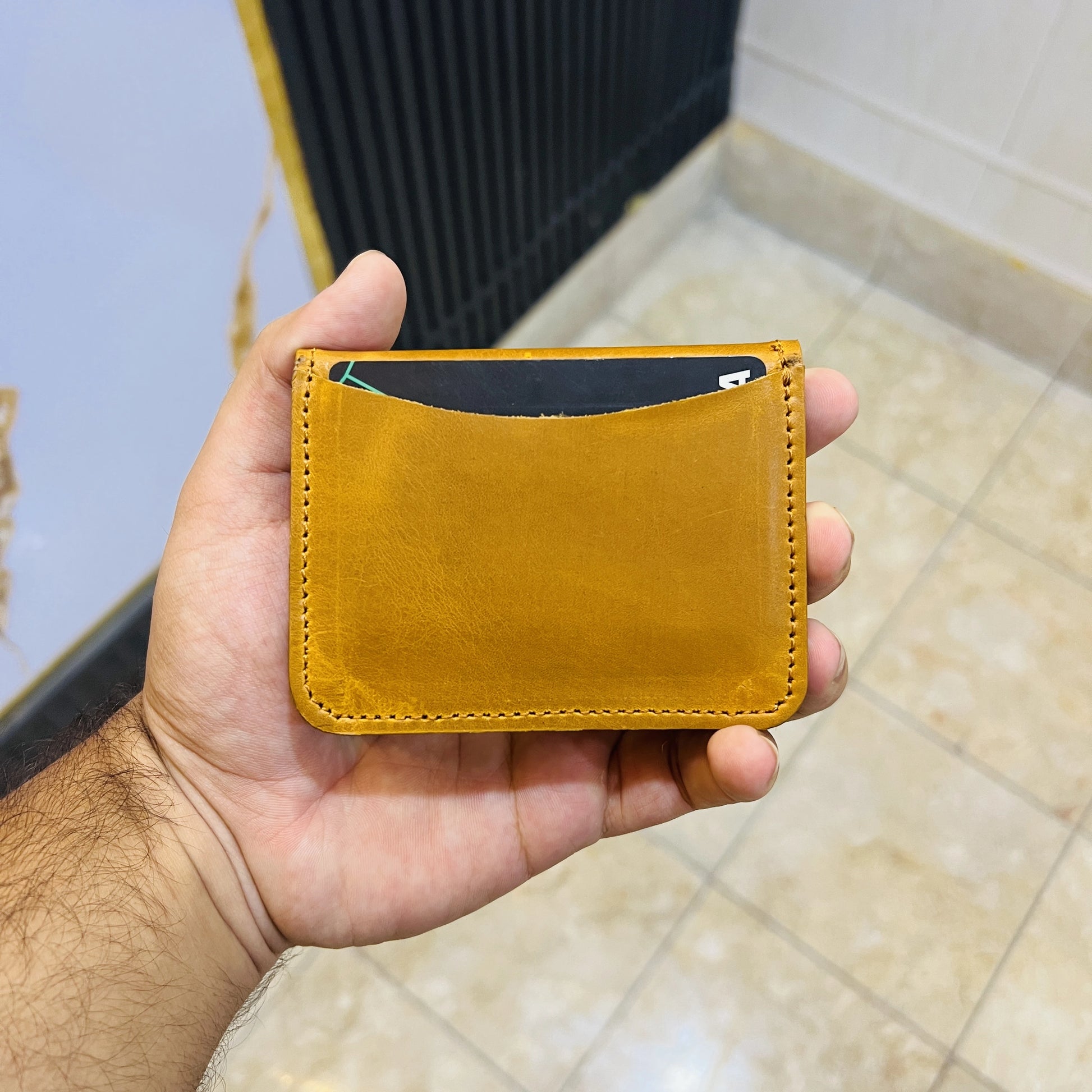 Hand holding a mustard yellow leather cardholder with a blurred background